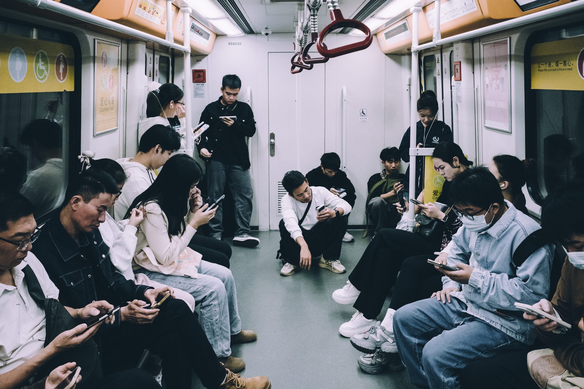 拥挤的地铁车厢内，每一位坐着的、站着的、蹲着的乘客都在低头看手机，画面里没有一双抬起的眼睛